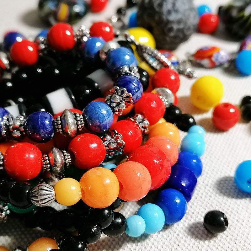 des bracelets très colorés en perles de Briare sont empilés sur un tissu écru